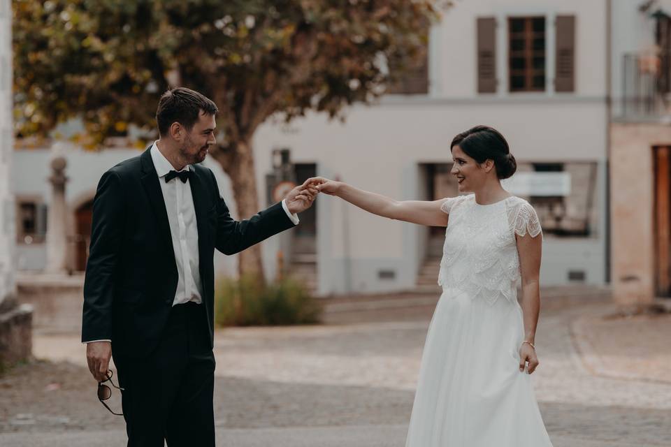 couple de futurs mariés homme et femme, vetus en tenue de mariahe, homme en costume noir et femme en robe de mariée blanche, le couple se regarde avec beaucoup de complicité et se donne une main tendue