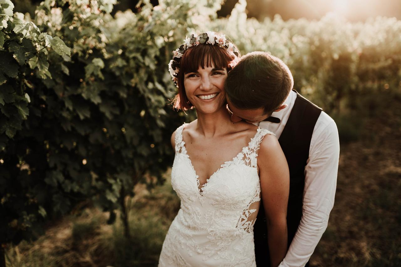 couple de mariés enlacés, la mariée porte une coiffure avec cheveux courts et une couronne de fleurs comme accessoire de tête