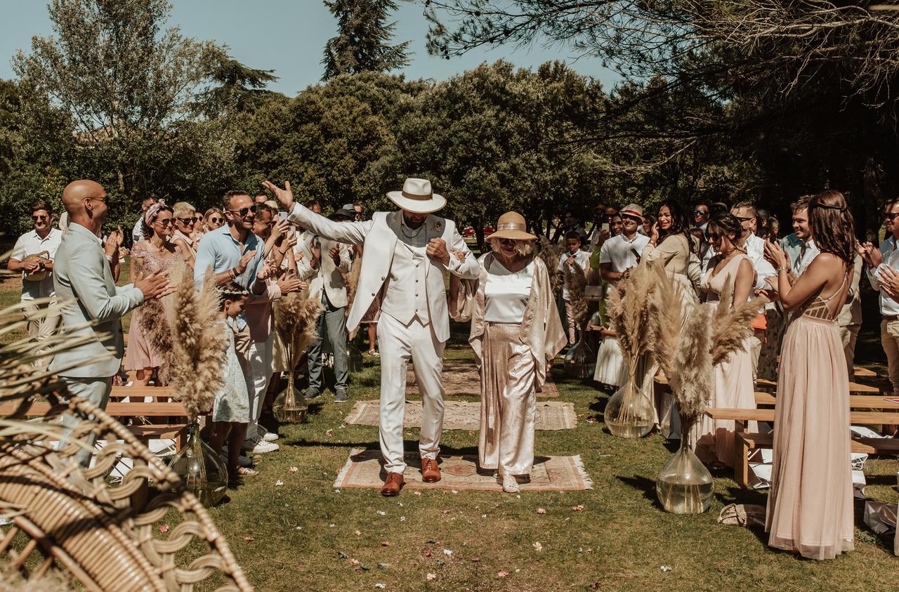 marié entre avec sa mère a la ceremonie de mariage, vetus de beige, tenue mere du marié champagne avec blouse blanche, les deux portent un chapeau de paille, mariage été
