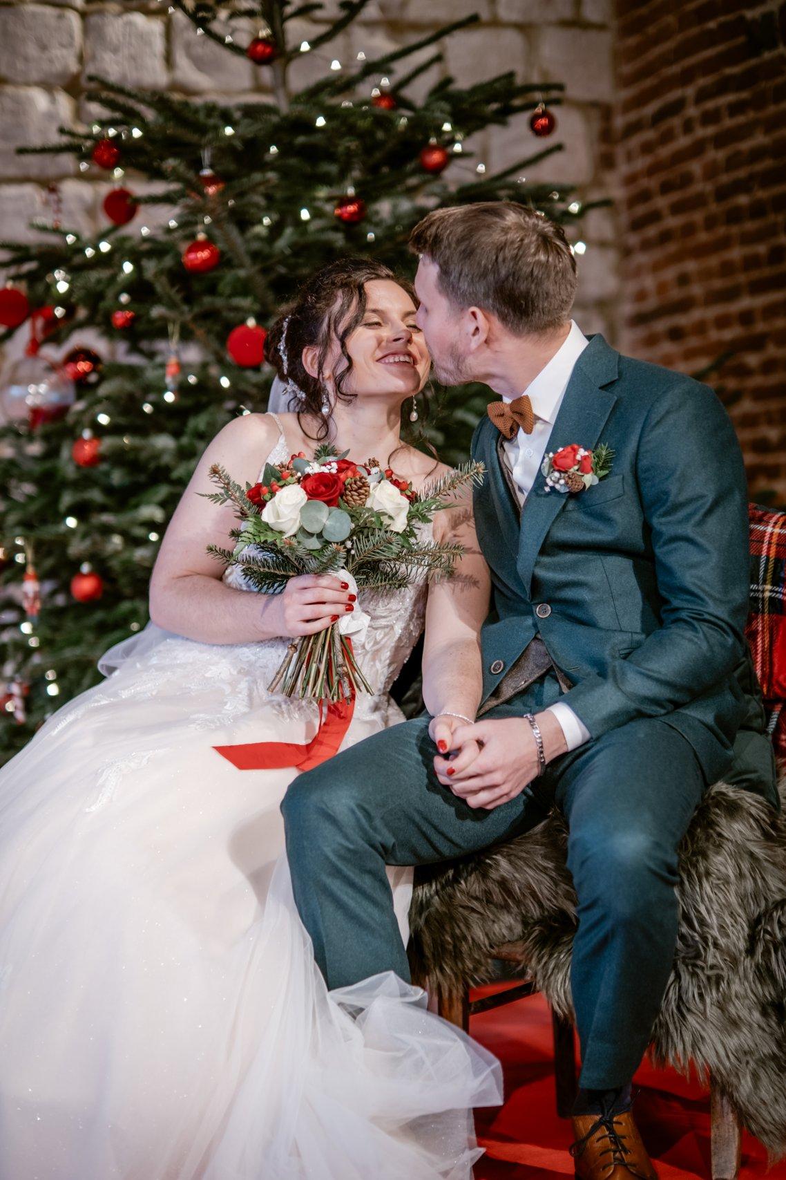 couple devant un sapin rouge et vert assorti au bouquet de la mariée