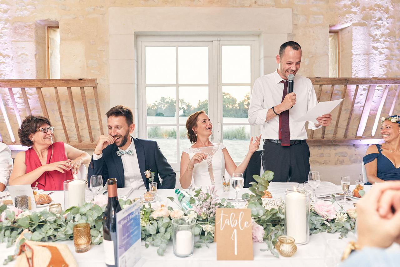discours temoin de mariage humour, temoin debout avec micro, mariés qui rigolent assis à table