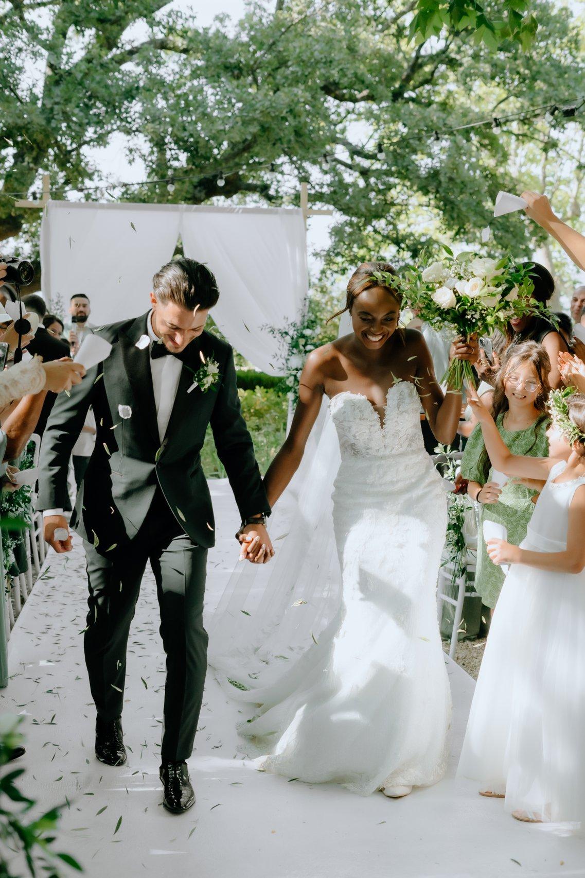 photo de couple main dans la main en costume et robe de mariée dans l'allée centrale de leur ceremonie laique