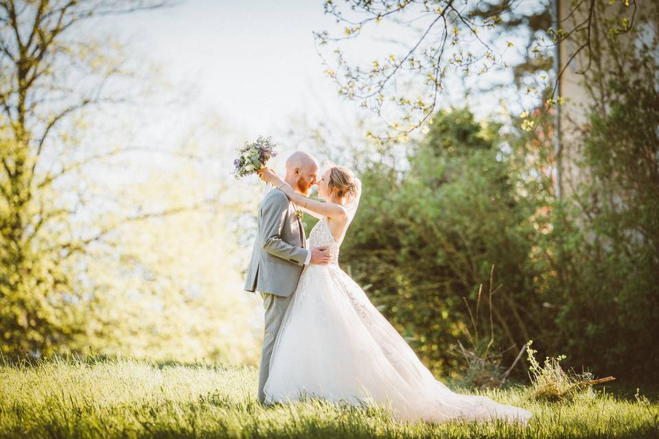 Seance de couple dans les bois, la mariée porte une robe princesse et un bouquet de fleur primtanier, le marié porte un costume gris