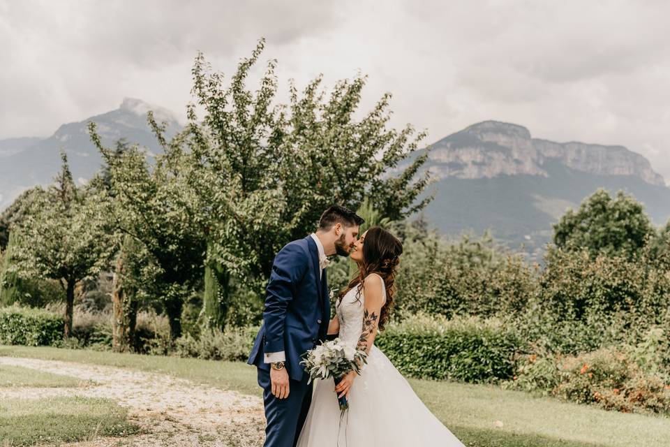 couple de mariés qui s'embrassent en pleine nature, lui en costume bleu, elle en robe de mariée blanche