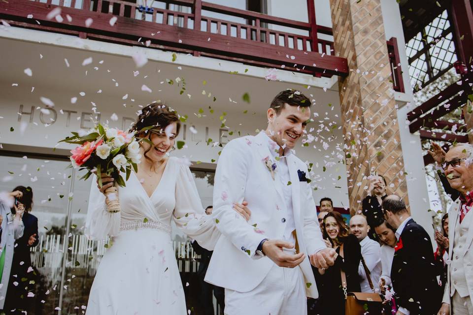 Sortie des mariés de l'hotel de ville la mariée porte une robe droite blanche et un bouquet de fleur à la main et le marié porte un costume blanc