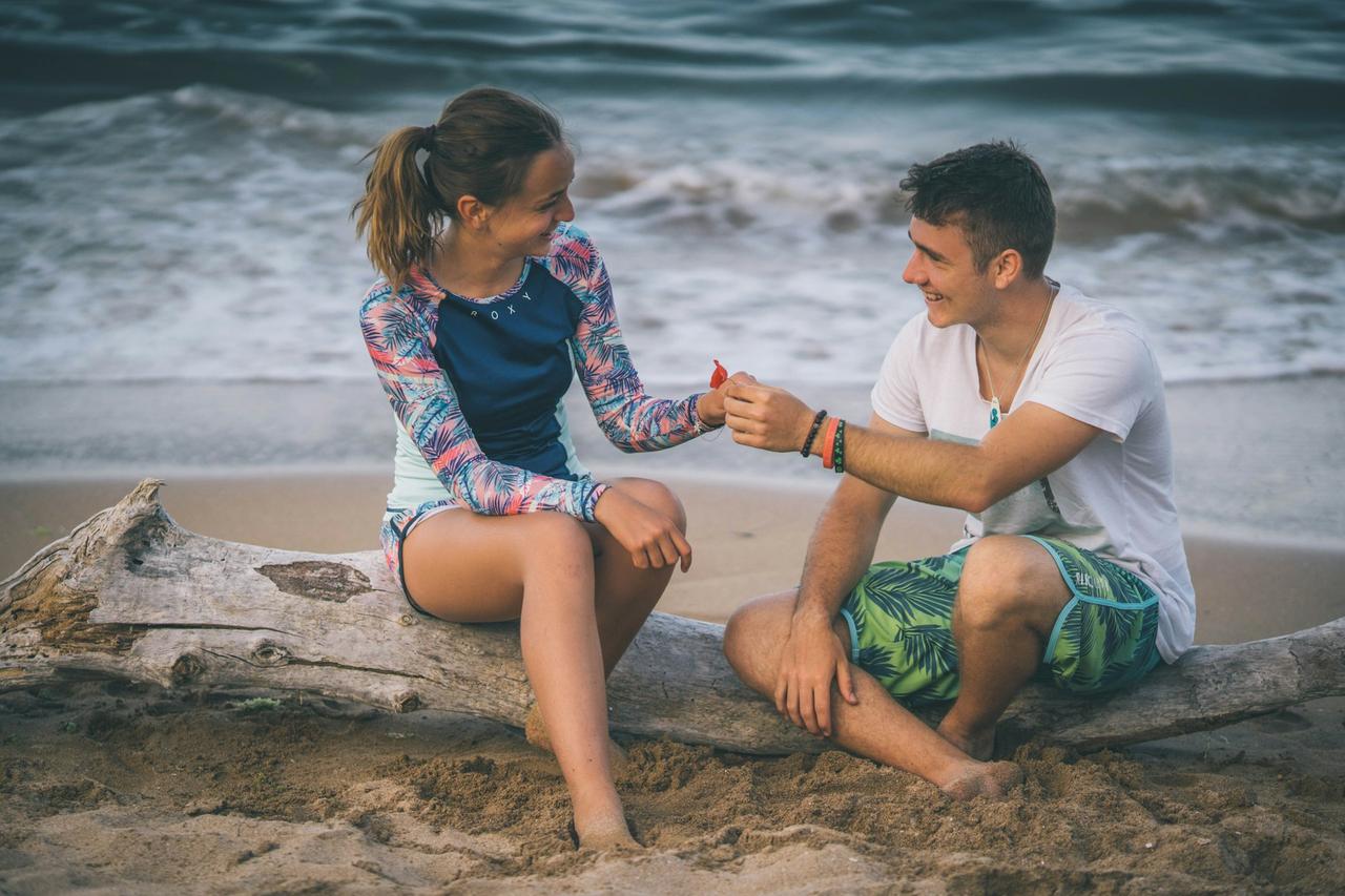 homme et femme assis sur la plage, questions à se poser en couple en vacances