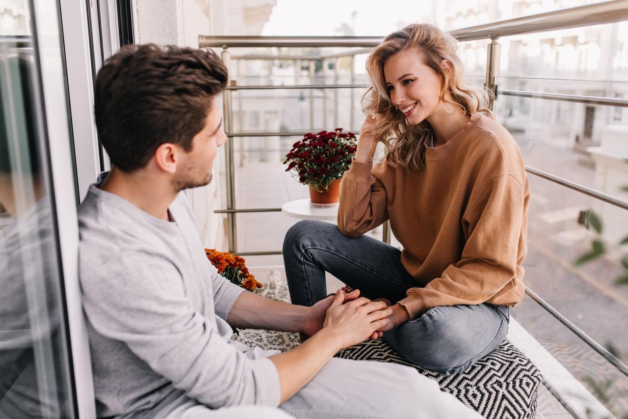 homme et femme qui parlent sur un balcon, homme prend les mains de la femme dans les siennes, seduction couple