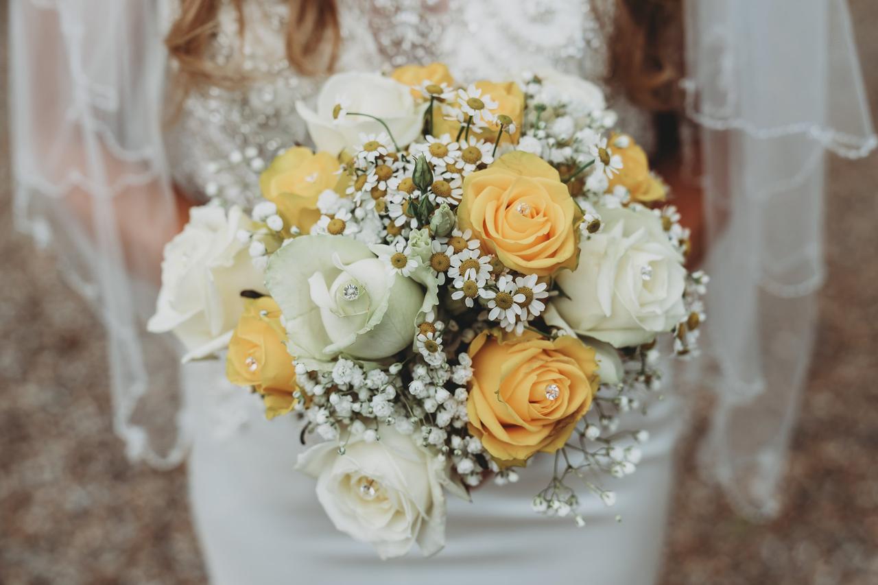 mariée qui porte un bouquet de fleurs blanches et jaune beurre avec marguerites