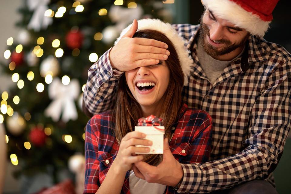 jeune femme qui rigole dont les yeux sont cachés par un jeune homme dans une ambiance de Noel