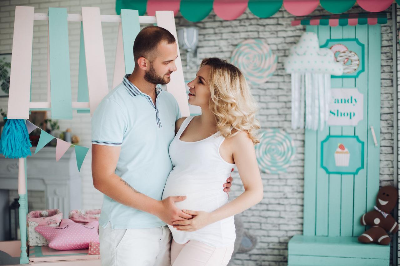 futurs parents debout, mari qui pose sa main sur le ventre arrondi de sa femme, baby shower, annonce naissance bébé