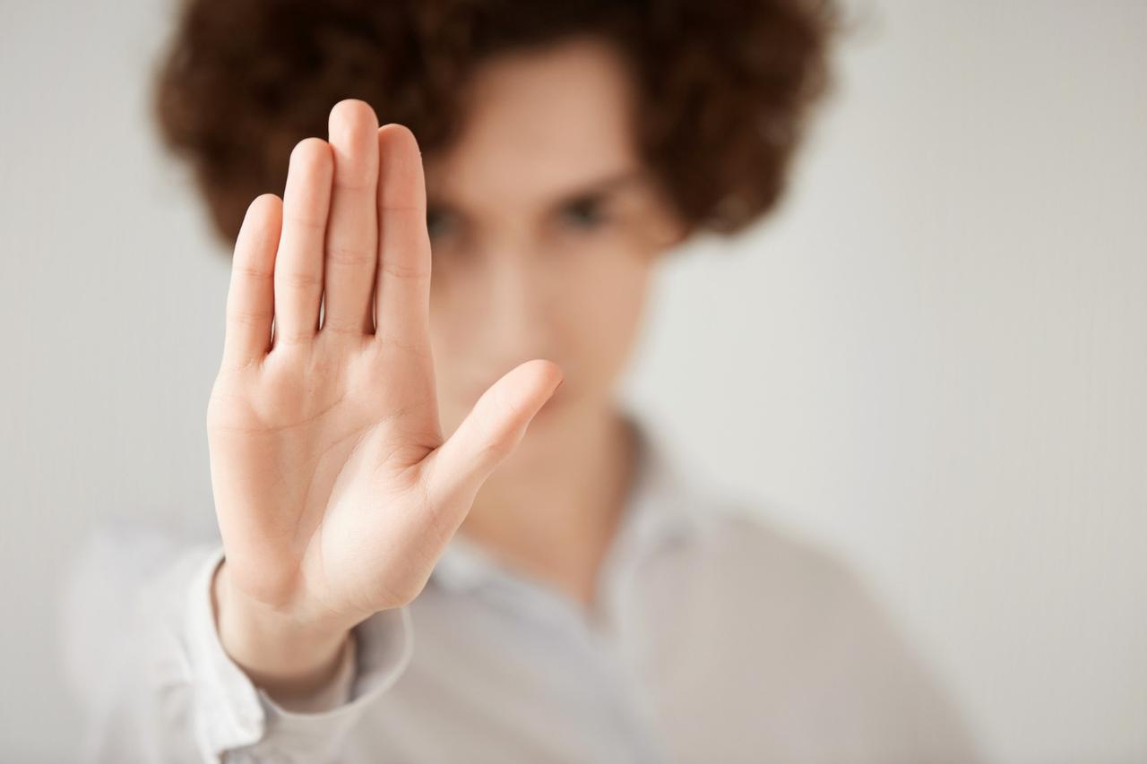 Une jeune femme brune aux cheveux bouclés qui fait signe STOP de la main, stop à la manipulation