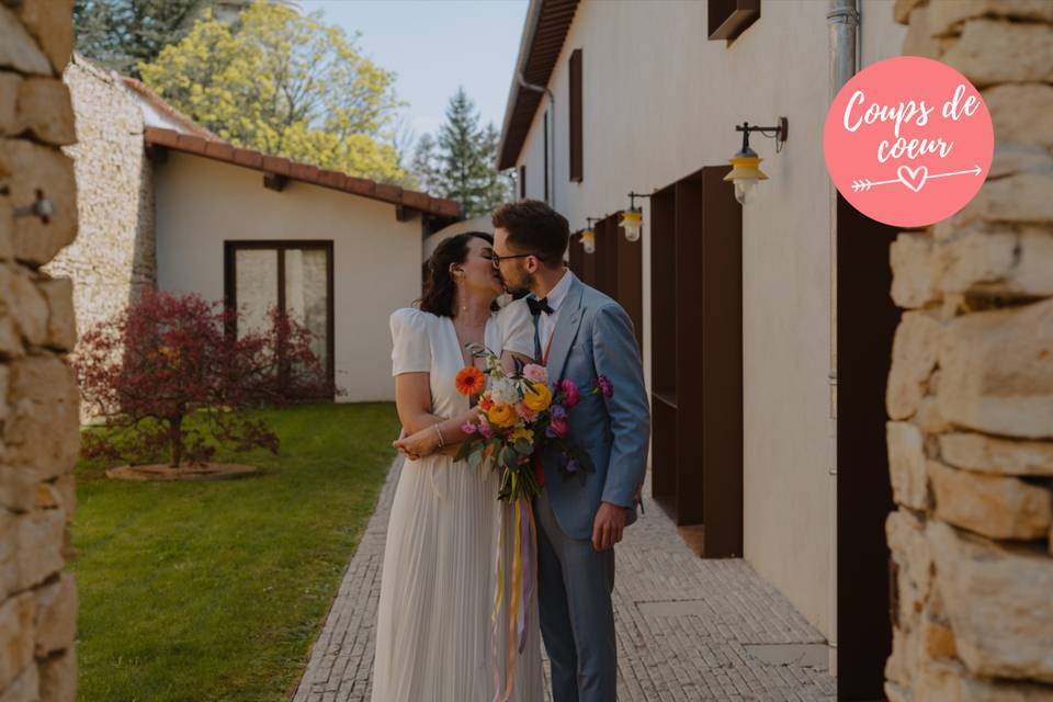 couple homme et femme qui s'embrasse, habillés de manière élégante, elle en robe et lui en costume de mariage, on observe une batisse derrière eux, lieu de mariage lyon