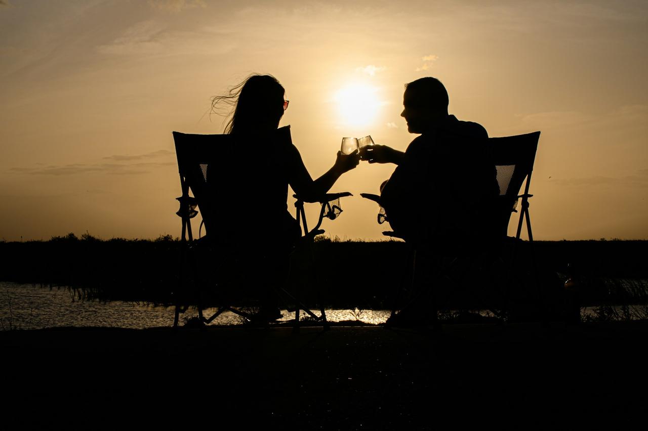 homme et femme assis face a la mer qui trinquent avec une coupe au coucher du soleil, questions à se poser en couple en vacances