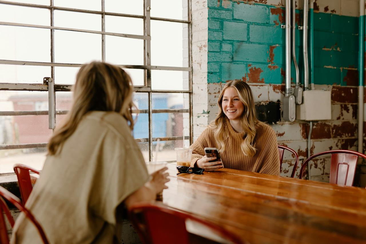 femme assise à une table avec téléphone portable, en face d'une autre femme, premier rendez-vous, 36 questions pour tomber amoureux d’Arthur Aron