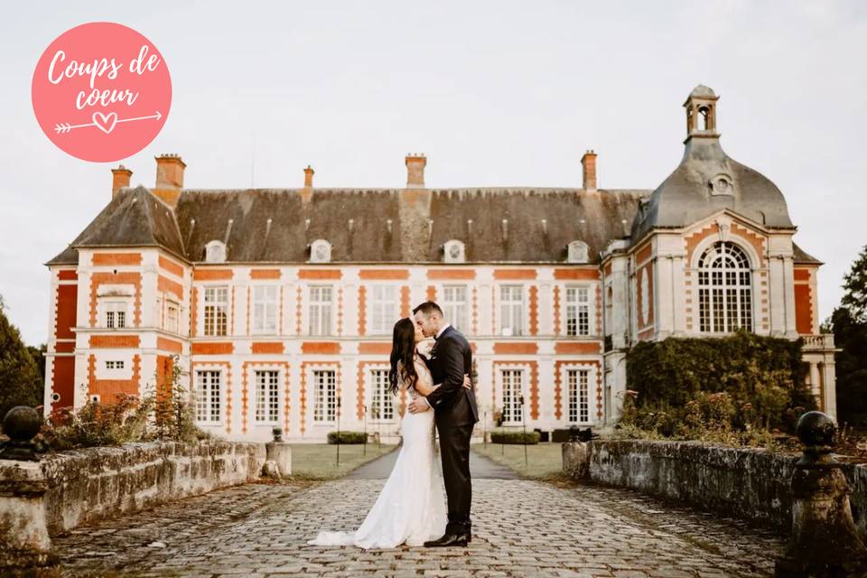 couple homme et femme en tenue de mariage, lui en costume elle en robe de mariée, devant un chateau prestigieux, lieu de réception grandiose