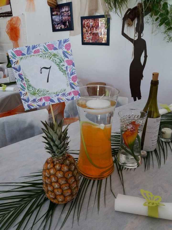 Ananas avec le numéro de table piqué dedans. Vase avec fleur immergée et bougie flottante dessus